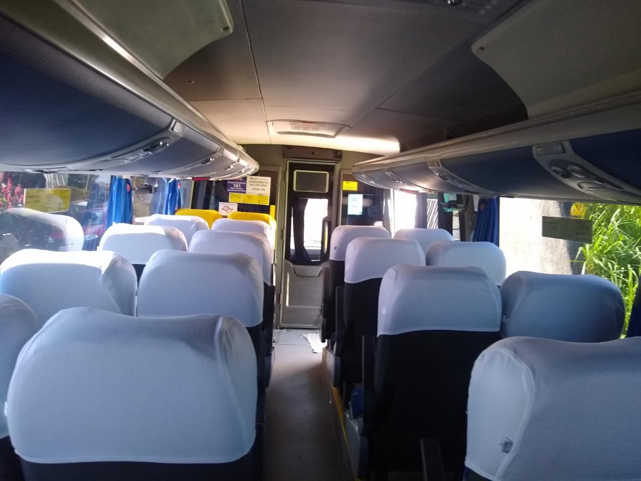 Interior do micro-ônibus com bancos de capas brancas, corredor central e bagageiros superiores